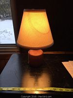 Small teak accent lamp with white textured clip-on shade illuminated, placed on a dark surface with measuring tape showing about 13 inches in height.