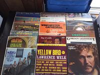 Photo showing Herb Alpert & Tijuana Brass and Lawrence Welk LP records, Gordon Lightfoot albums on top of a black surface with a blue container in background.
