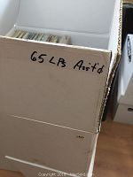 Photo of cardboard box labeled '65 LP Ass't'd' containing LP records upright inside.