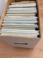 Box filled with approximately 135 comic books in plastic sleeves, viewed from above.