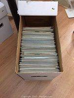 View of comic books stored upright in a large white cardboard storage box showing the edges of comic covers and pages.