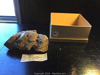 Photo showing the rock specimen with feldspar crystals next to a box and a label indicating sample information