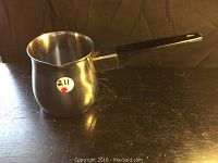 Stainless steel milk pot with handle placed on dark surface, shows overall shape and size.