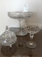 Front view of all three crystal pieces on table: a large footed fruit bowl, a smaller footed candy dish, and a covered footed candy dish.
