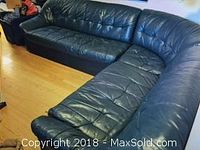 Angled front view of full L-shaped blue leather sectional on hardwood floor under artwork