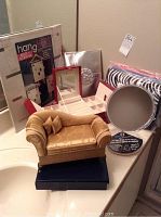 Photo of assorted jewelry organizers, adjustable mirror, scarf hanger organizer in packaging, and miniature gold sofa-shaped jewelry holder on a bathroom counter.