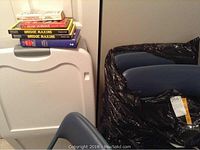Photo showing the stack of bridge books on top of the white Sterilite storage container with wheels next to four navy blue padded folding card table chairs.