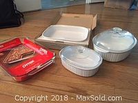 Photo showing two Pyrex clear glass oblong baking dishes and three white ceramic Corning Ware French White baking dishes with lids on a floor.