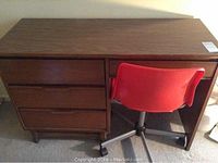 Mid-century desk with red Ikea swivel chair pushed underneath.