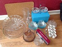 Overview of entire lot showing various glass and crystal serving dishes, including the Birks candy dish on blue box, blue Bohemian fruit bowl, egg cups, cheese dish, and silver plated ice shovel in box.