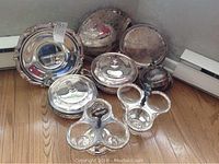Overview of all silver plated items including covered casseroles, trays, condiment servers, and serving pieces arranged on floor.