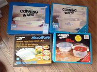 Four boxed Corning Ware dishes shown: roaster, covered saucepot, microwave cooker with built-in rack, and cookware set with covers