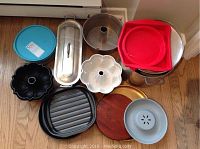 Overview photo showing various silicone, metal, and wooden baking items arranged on floor including bundt pans, loaf pan, and large pot.