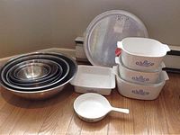 All items in the lot include the nested stainless steel mixing bowls, CorningWare glass bakeware, ceramic saucepan, and metal pizza pan.