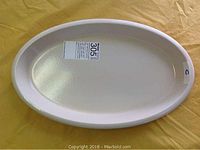 Top view of oval shallow bakeware dish showing off-white interior with sticker on bottom.