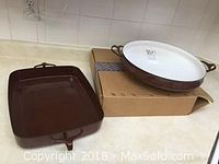 Both items side by side: round paella pan resting on box and rectangular brown lasagna dish