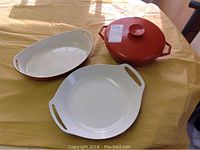 Three Copco ceramic dishes arranged on table: round covered dish with orange lid, round open dish with handles, and oval dish with handles.