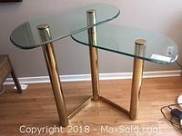 Two-tiered glass top console table with brass legs viewed from an angle showing the shape and condition of the glass surfaces.