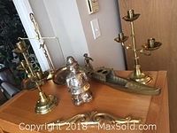 Lot contents on a wooden surface showing brass candelabras, brass weighing scale, Bobby bank, and brass tray.