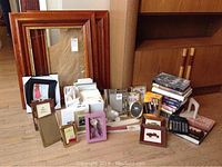 Full view of assortment of wooden and metallic picture frames, stack of books, calculator, and framed embroidery.