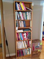 Photo of wooden shelving unit filled with books and two cardboard boxes placed on the floor beside it.