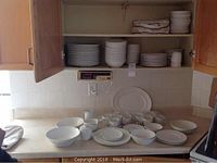 Wide view of countertop and open cabinets showing stacks of plates, bowls and cups