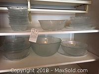 Multiple clear glass dishes including bowls, plates, and platter on shelves