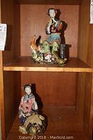 Photo of the two Asian figurines displayed on a wooden shelf, showing size and positioning.