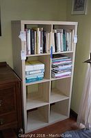 Front view of the shelving unit filled partially with books, showing 8 cubby compartments in a blonde wood finish.