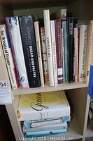 Shelf with various hardcover and softcover books on baking, cooking, knitting, painting, and crafts.