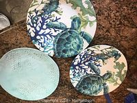 Three ceramic plates, two with sea turtle and coral designs and one textured seafoam green plate.