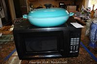 Microwave oven with Le Creuset rondeau placed on top, showing overall view of both items.