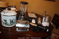 Full view of cooking pot, blender, pasta maker, food processor, food saver bags and rolling pin on table