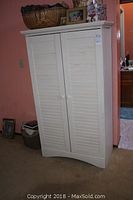 Closed view of light-colored armoire with plantation shutter doors and round knobs