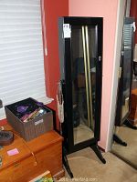 Full view of the black cheval mirror jewelry case on stand, showing height and placement near corner of room.