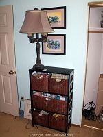 IKEA black laminate shelving unit with five brown wicker baskets filled with various items, positioned against a wall next to a door