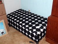 Storage ottoman resting on floor next to wooden cabinet, showing full top and sides with black and white polka dot pattern upholstery.