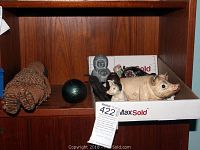 Shelf holding multiple figurines and a box containing various pig figurines and an Eskimo statue, showing a painted iron piggy bank and ceramic items.