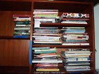 Wide view of multiple stacked books on wooden shelves, mixture of cooking and craft related titles.