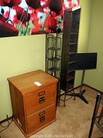 Wooden filing cabinet and two metal CD racks positioned against wall with red floral wall art
