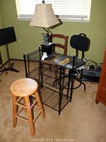 Lot image showing the wooden stool, black metal chair, wooden chair with wicker seat, and resin parrot lamp on black metal shelving unit.