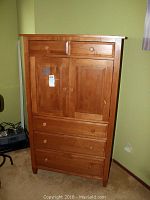 Front view of wood armoire showing drawers and cabinet doors with round wooden knobs.