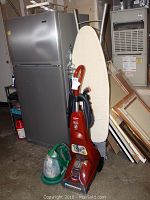 Photo showing Bissell Powersteamer upright steam cleaner in front of a refrigerator, with a green Bissell Little Green portable cleaner beside it and an ironing board in the background.