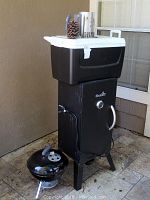 Charbroil smoker with white and black cooler on top and small Weber kettle BBQ beside it, showing overall setup and items included
