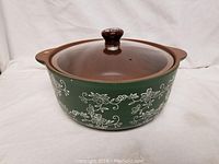 Green and white floral patterned stove top baker with brown glass lid and knob photographed from the side.