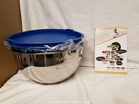 Main image showing large nested stainless steel bowls with blue plastic lids on top, placed on white cloth background.