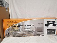 Box label showing Kross branding, compatibility for 32"-70" LCD and plasma TVs, and key features including swivel up to 90° and tilt up to ±15°. Also mentions weight capacity of 65 kg (143.3 lbs) and included mounting hardware.