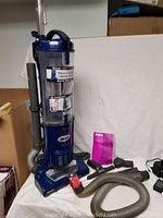 Full view of the Shark Navigator Swivel Plus vacuum upright with attached hose, various attachments, and user manual displayed.