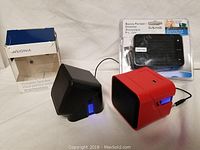 Two cube-shaped portable speakers, one black and one red, both with illuminated power indicators shown on a white background.