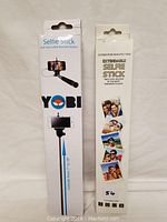 Two boxed YOBI brand extendable selfie sticks with aux cable remote shutter, shown from front and back packaging views.